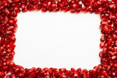 Frame made of ripe juicy pomegranate grains on white background, top view. Space for text