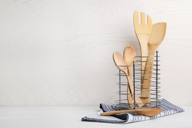 Holder with wooden kitchen utensils and napkin on table. Space for text