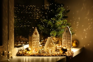 Photo of Beautiful decorative houses, baubles and small Christmas tree on window sill indoors