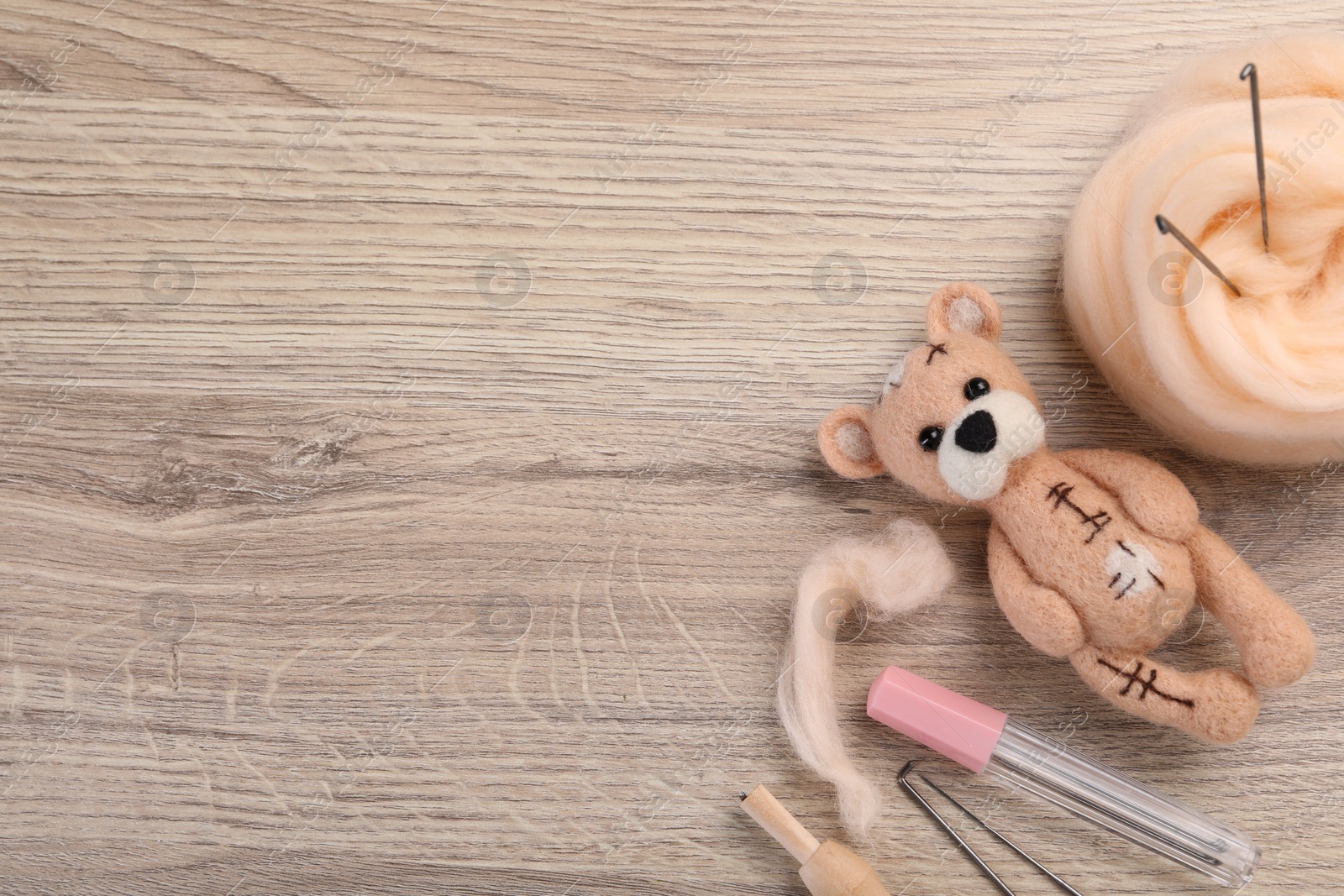 Photo of Felted bear, wool and tools on wooden table, flat lay. Space for text