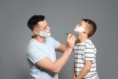 Photo of Dad pretending to shave his son with razor on grey background