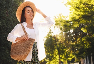 Young woman with stylish straw bag in park. Space for text