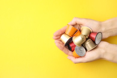 Woman holding heap of coffee capsules on yellow background, top view. Space for text