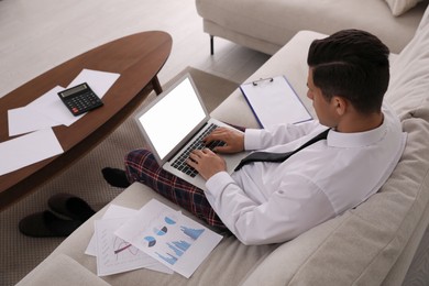 Photo of Man in shirt and pajama pants working on laptop indoors. Stay at home concept