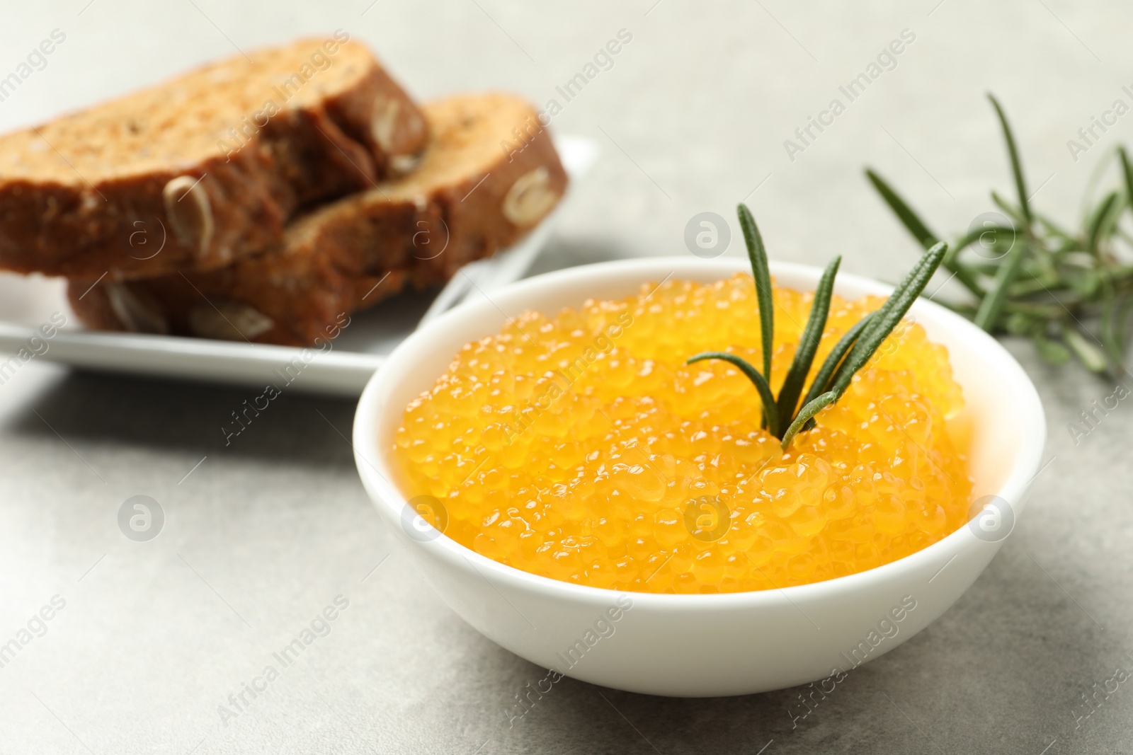 Photo of Fresh pike caviar in bowl, bread and rosemary on light grey table, closeup