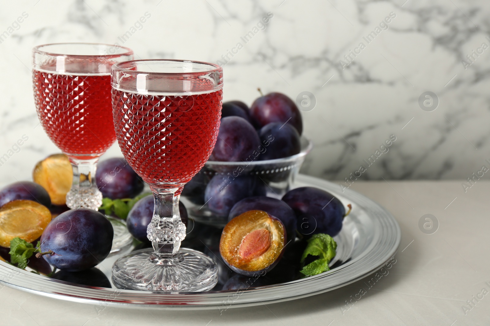 Photo of Delicious plum liquor, mint and ripe fruits on white table. Homemade strong alcoholic beverage