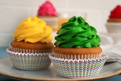 Delicious cupcakes with colorful cream on plate, closeup