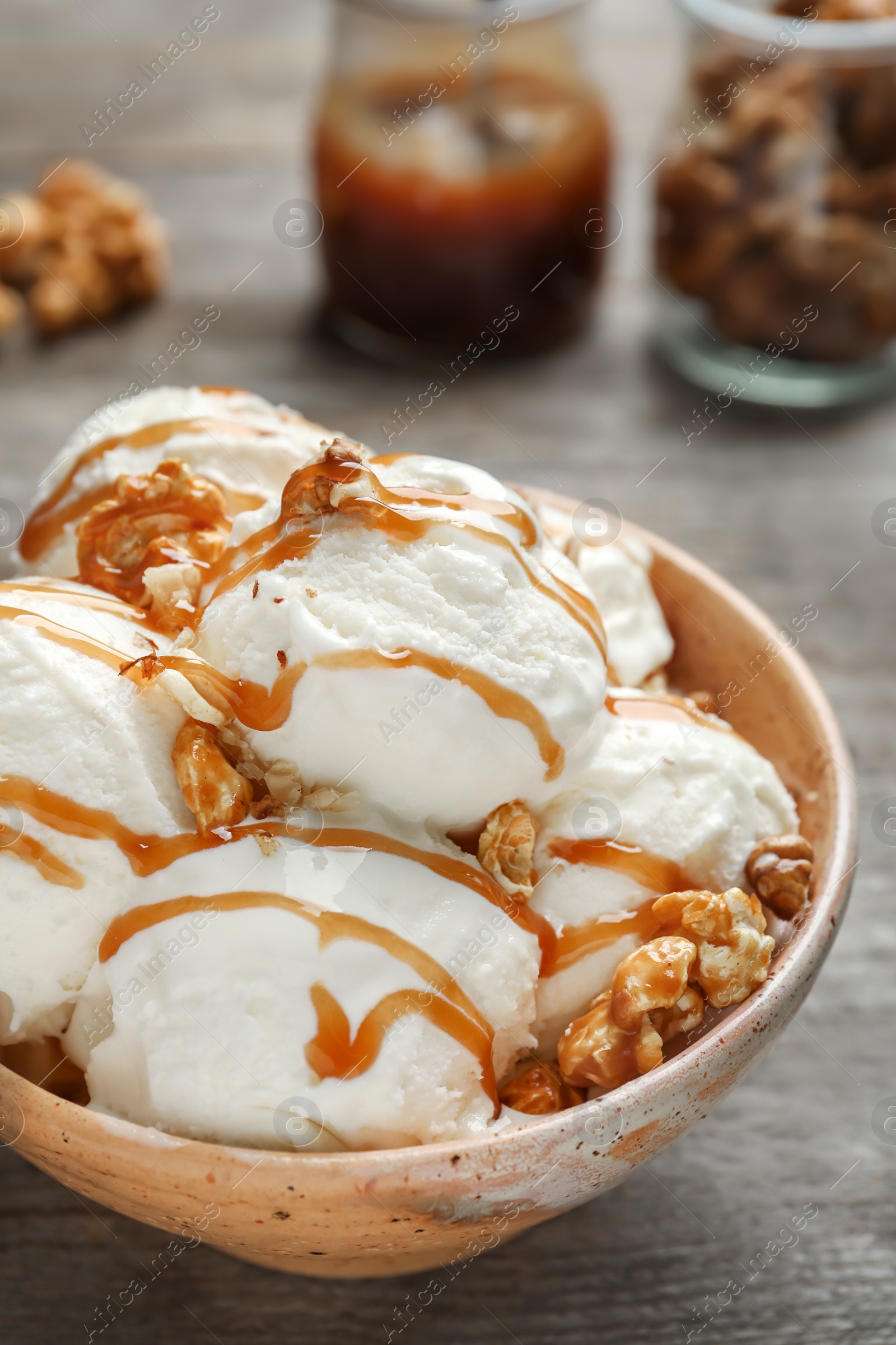 Photo of Tasty ice cream with caramel sauce and popcorn in bowl on wooden table