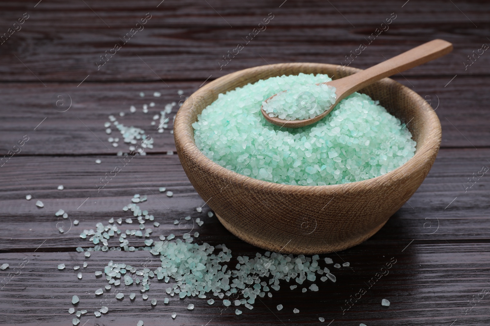 Photo of Bowl and spoon with turquoise sea salt on dark wooden table, closeup