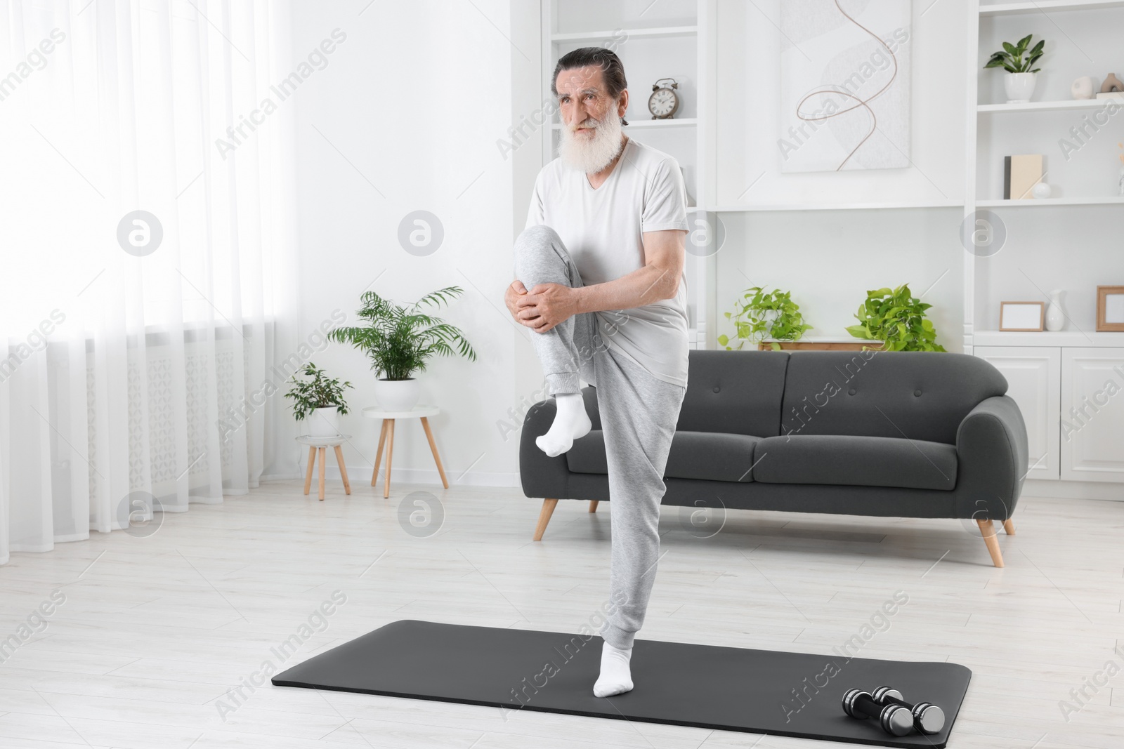 Photo of Senior man in sportswear stretching on mat at home