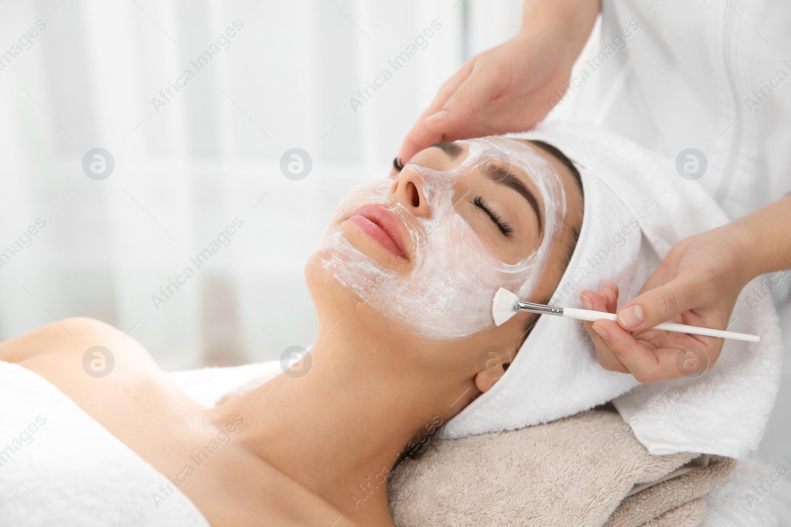 Photo of Cosmetologist applying mask on client's face in spa salon