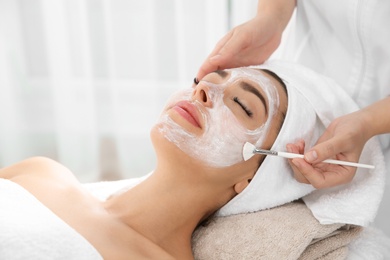 Photo of Cosmetologist applying mask on client's face in spa salon