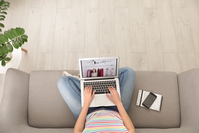 Photo of Woman holding laptop with open beauty blogger site on sofa, above view