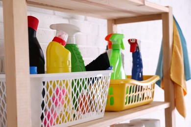 Photo of Many different detergents on wooden shelf near white brick wall