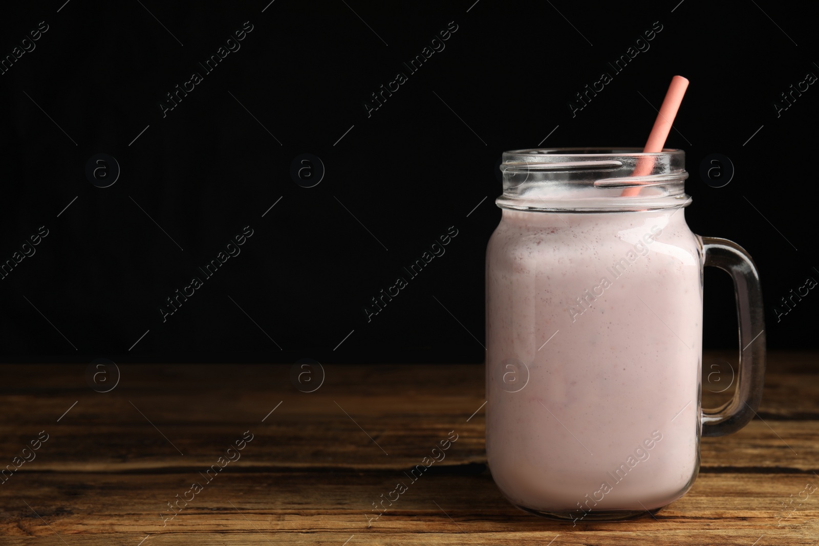 Photo of Tasty milk shake with straw in mason jar on wooden table. Space for text