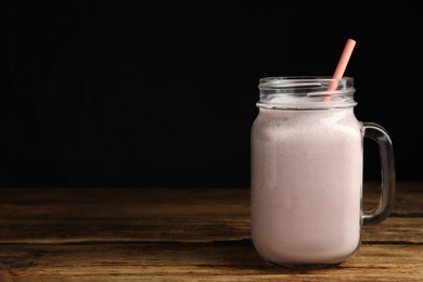 Photo of Tasty milk shake with straw in mason jar on wooden table. Space for text