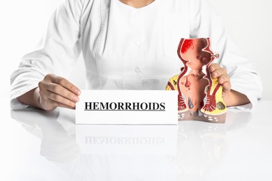 Photo of Doctor holding card with word Hemorrhoids and model of unhealthy lower rectum on white background, closeup