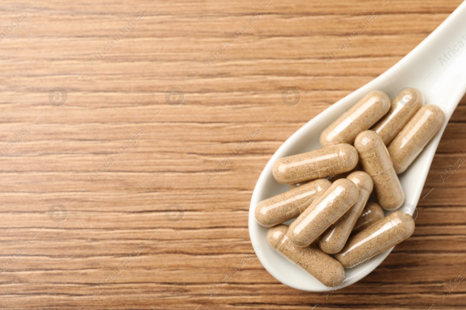 Photo of Spoon with dietary supplement capsules on wooden table, top view. Space for text