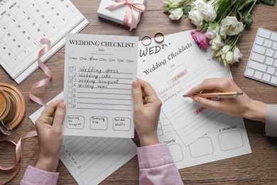 Photo of Women filling Wedding Checklists at wooden table, top view