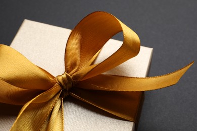 Photo of Golden gift box with satin bow on black background. closeup