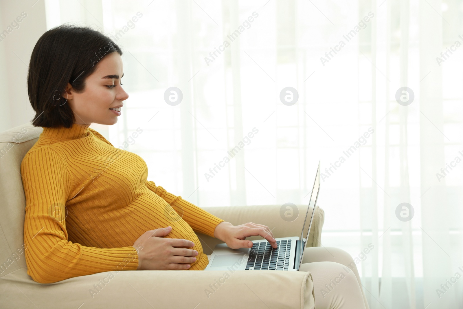 Photo of Pregnant young woman with laptop at home, space for text