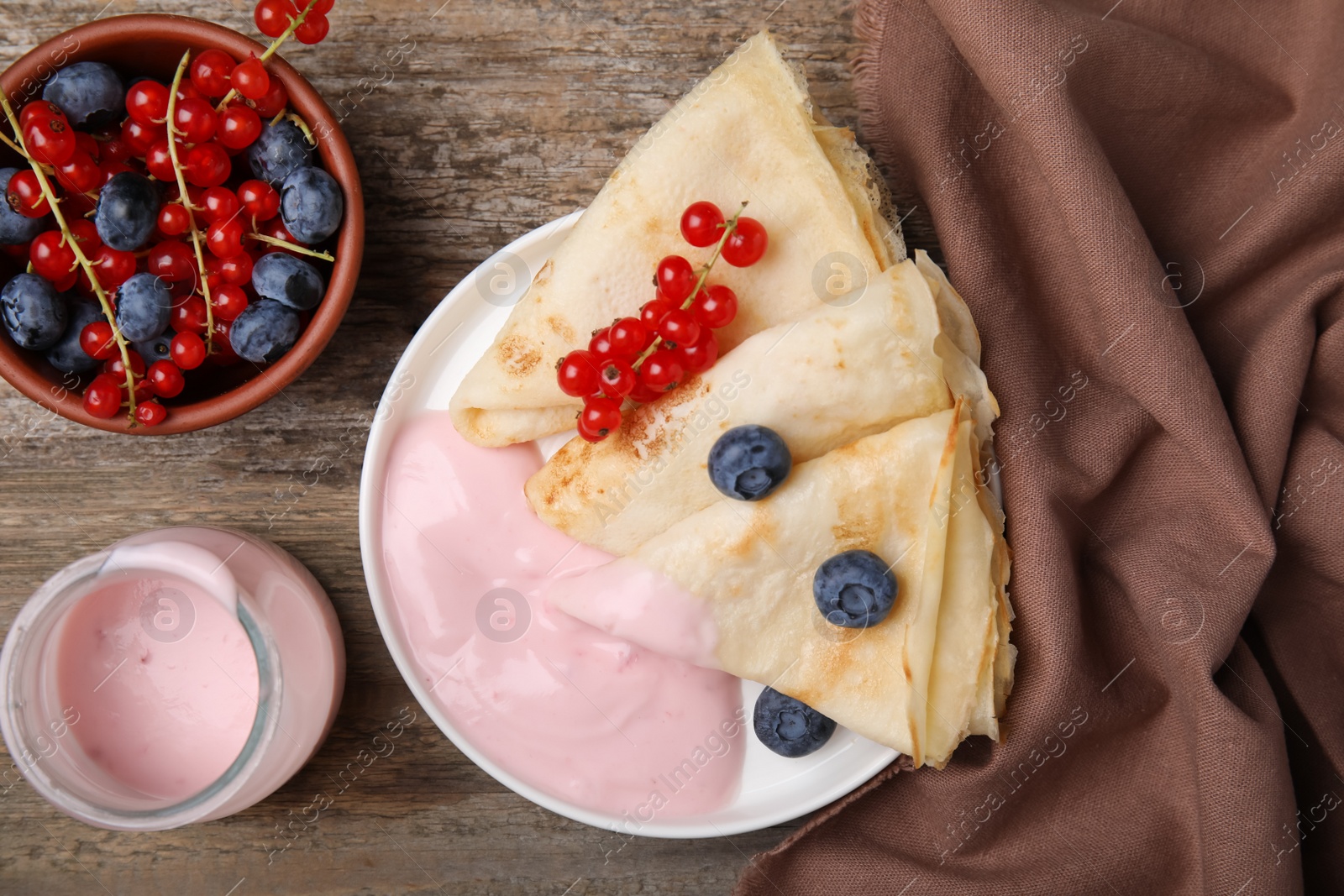 Photo of Delicious crepes with natural yogurt, blueberries and red currants on wooden table, flat lay