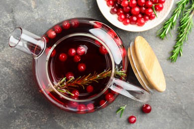 Photo of Tasty hot cranberry tea in teapot, rosemary and fresh berries on light grey textured table