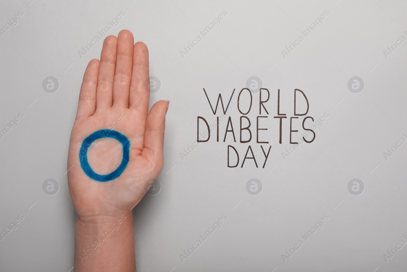 Photo of Woman showing palm with blue circle near text World Diabetes Day on light background, closeup