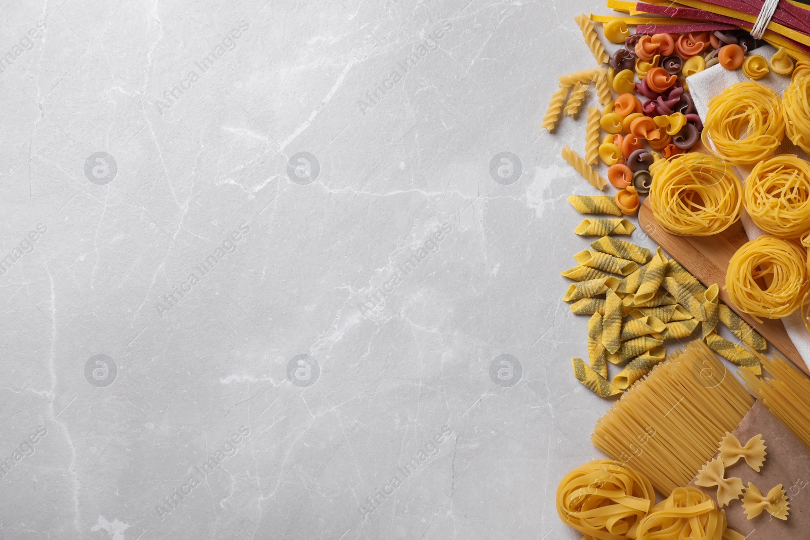 Photo of Different types of pasta on light grey marble table, flat lay. Space for text