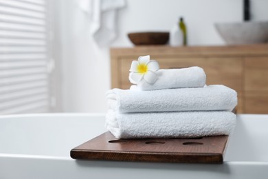 Photo of Stacked bath towels and beautiful flower on tub tray in bathroom. Space for text