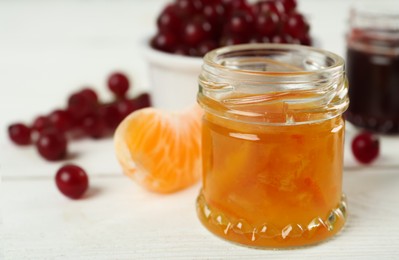 Photo of Open glass jar of sweet jam on white wooden table, closeup. Space for text