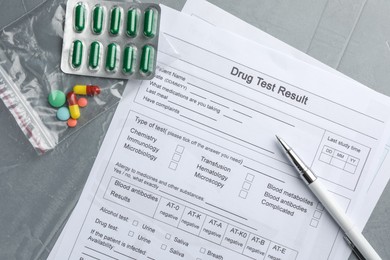 Photo of Drug test result form, pills and pen on grey table, flat lay