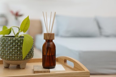 Aromatic reed air freshener near houseplant on wooden tray indoors. Space for text