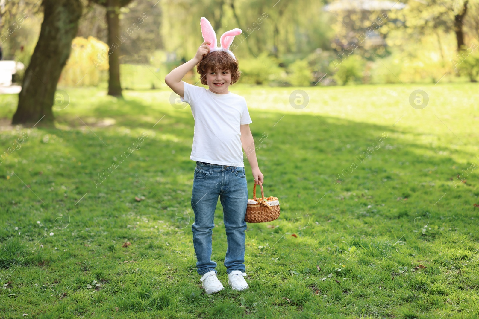 Photo of Easter celebration. Cute little boy in bunny ears holding wicker basket outdoors