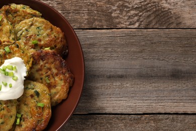 Photo of Delicious zucchini pancakes with sour cream and green onion on wooden table, top view. Space for text