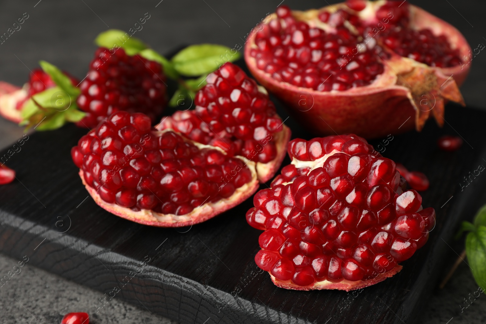 Photo of Cut fresh pomegranate and green leaves on grey table, closeup