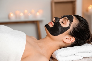 Beautiful woman with black mask on face relaxing in spa salon