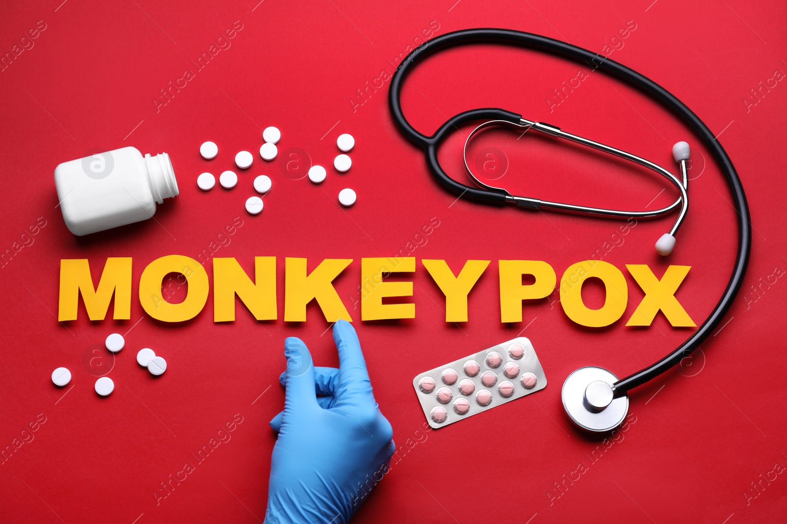 Photo of Nurse making word Monkeypox of paper letters, pills and stethoscope on red background, top view