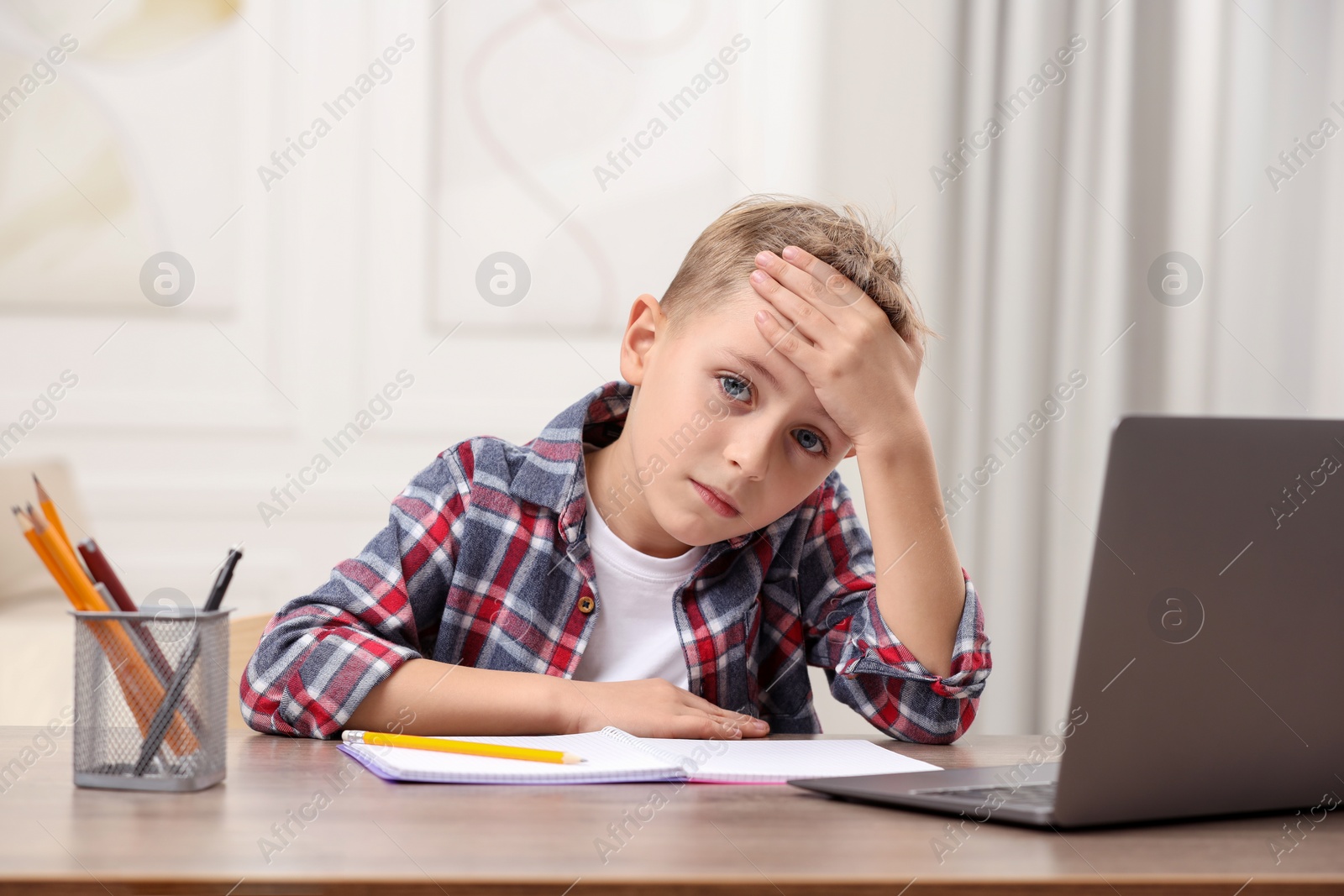 Photo of Little boy suffering from headache at wooden desk indoors