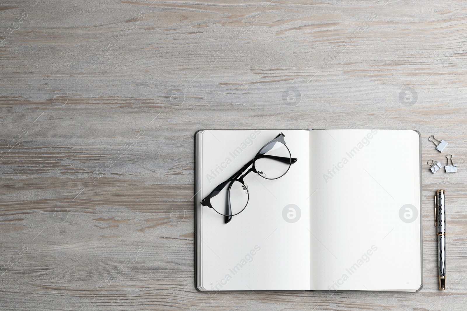 Photo of Ballpoint pen, notebook and glasses on wooden table, flat lay. Space for text