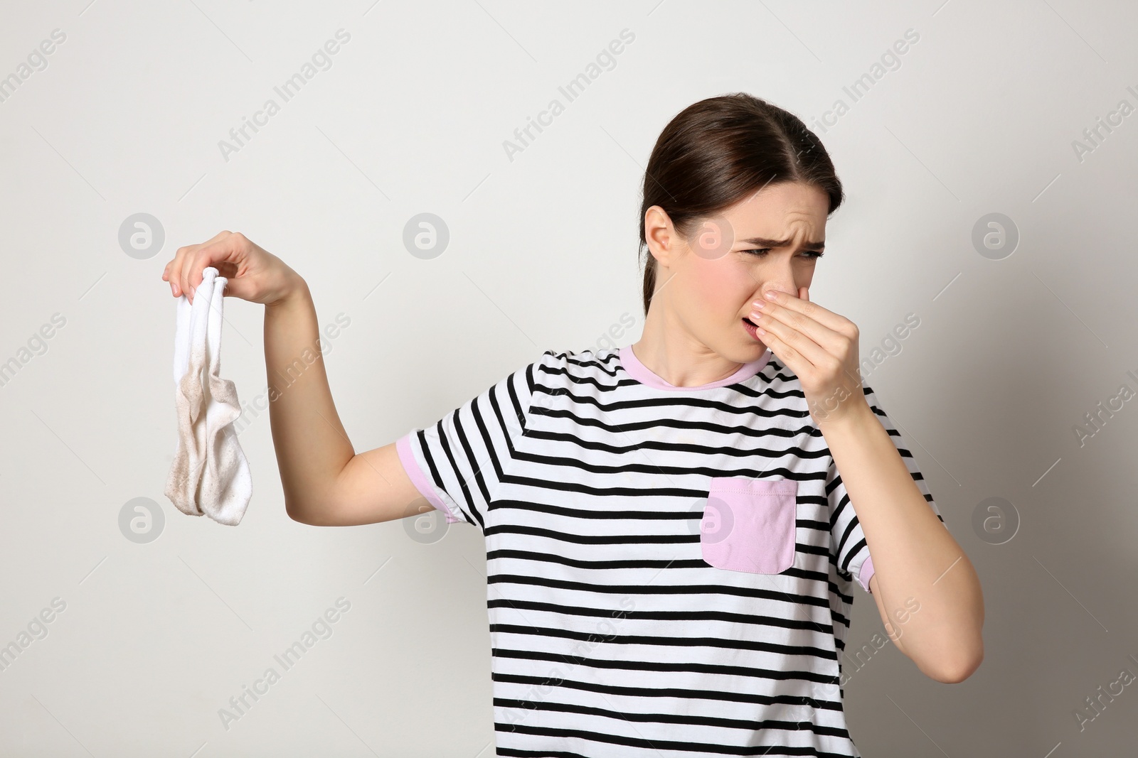 Photo of Young woman feeling bad smell from dirty socks on light grey background