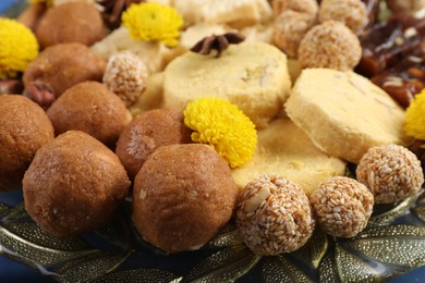 Diwali celebration. Tasty Indian sweets and chrysanthemum flowers on plate, closeup