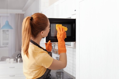 Woman cleaning microwave oven with rag in kitchen