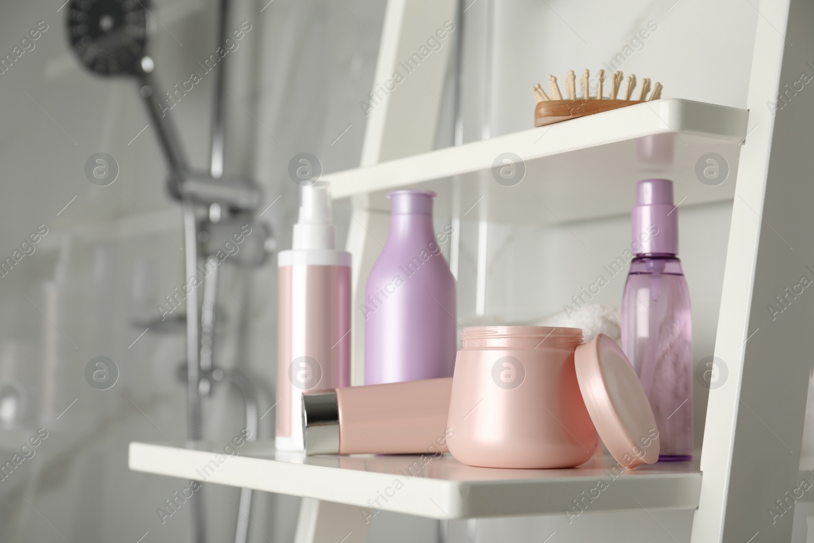 Photo of Different hair care products and brush on shelving unit in bathroom