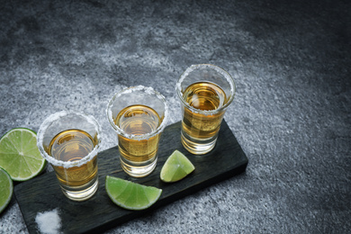 Photo of Mexican Tequila shots, lime slices and salt on grey table