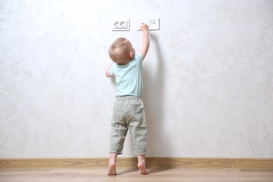 Little child playing with electrical socket indoors, back view. Dangerous situation