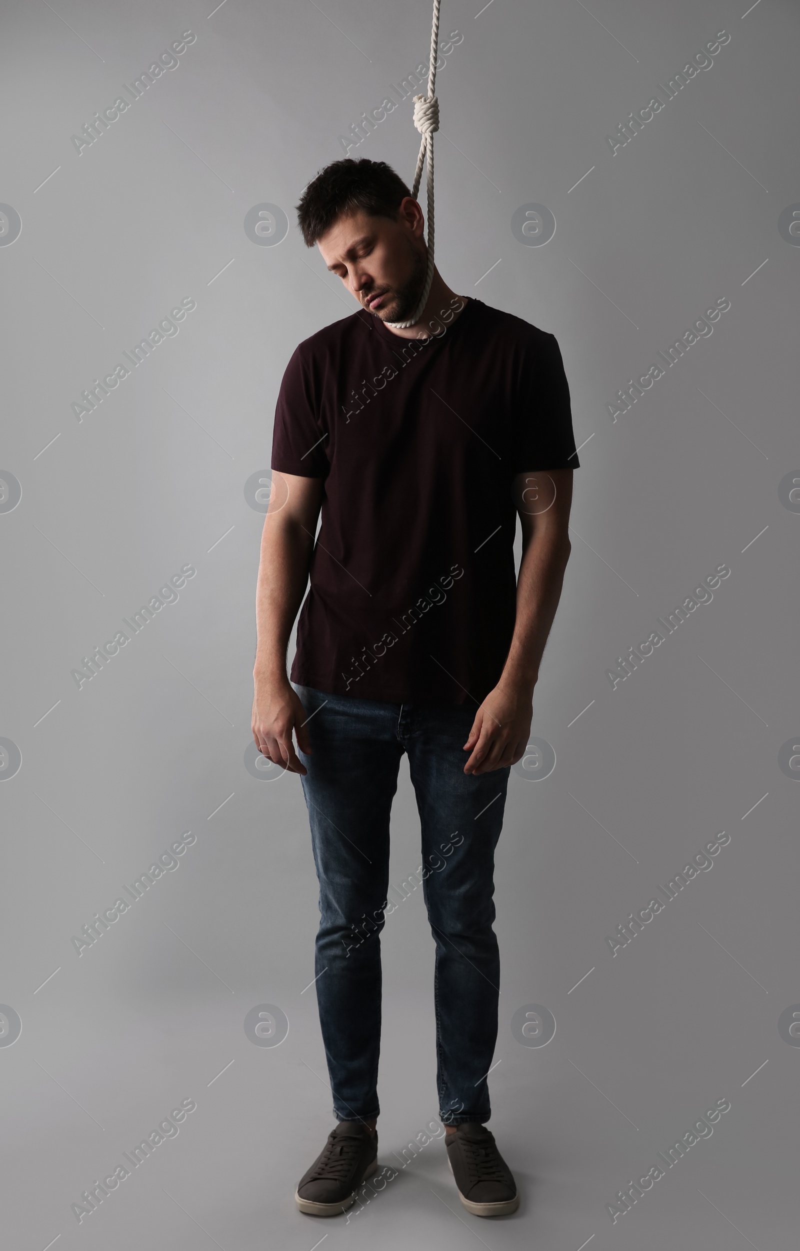 Photo of Depressed man with rope noose on neck against light grey background