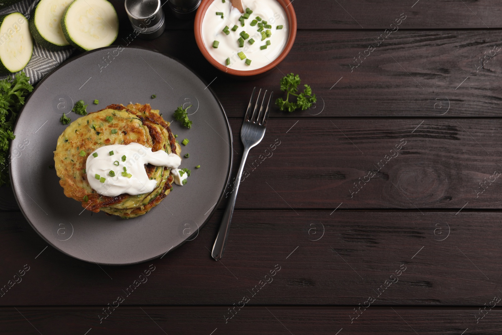 Photo of Delicious zucchini fritters with sour cream on wooden table, flat lay. Space for text