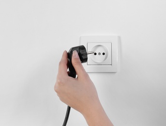 Photo of Woman putting plug into power socket on white background, closeup. Electrician's equipment
