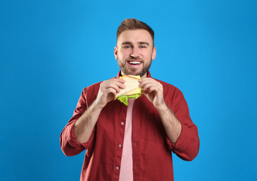 Young man with tasty sandwich on light blue background